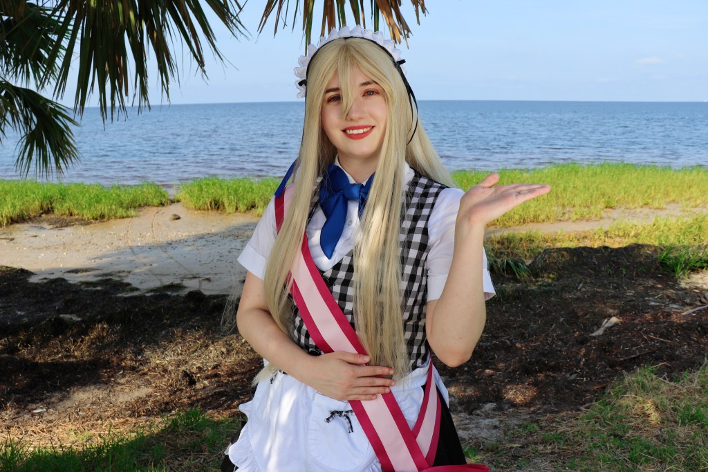 An image of a woman wearing a maid costume standing under palm trees at the beach.